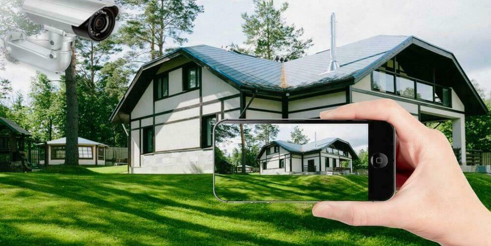 Видеонаблюдение для частного дома На фоне частного дома уличая видеокамера и смартфон с картинкой этого дома