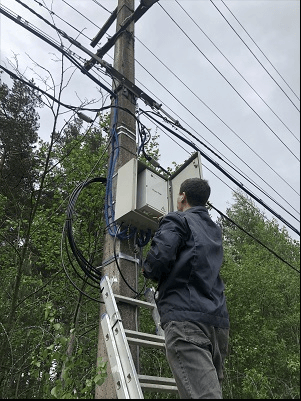 Мастер стоя на лестнице, в слаботочном щите , установленном на столбе, настраивает компоненты видеонаблюдение