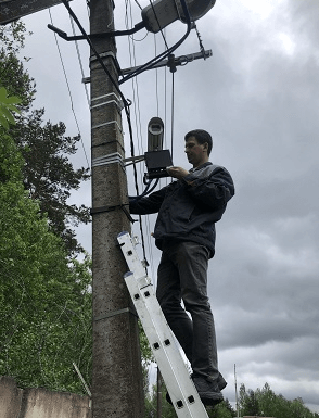 Специалист, стоит на лестнице и ремонтирует видеокамеру закрепленную на столбе